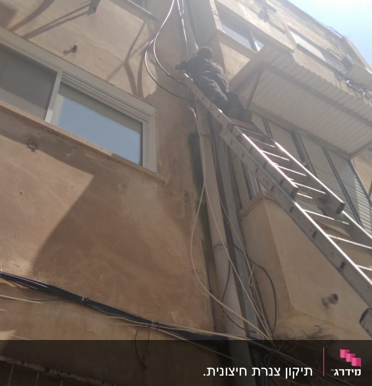 אדם על סולם מתקן צינורות על קיר בניין